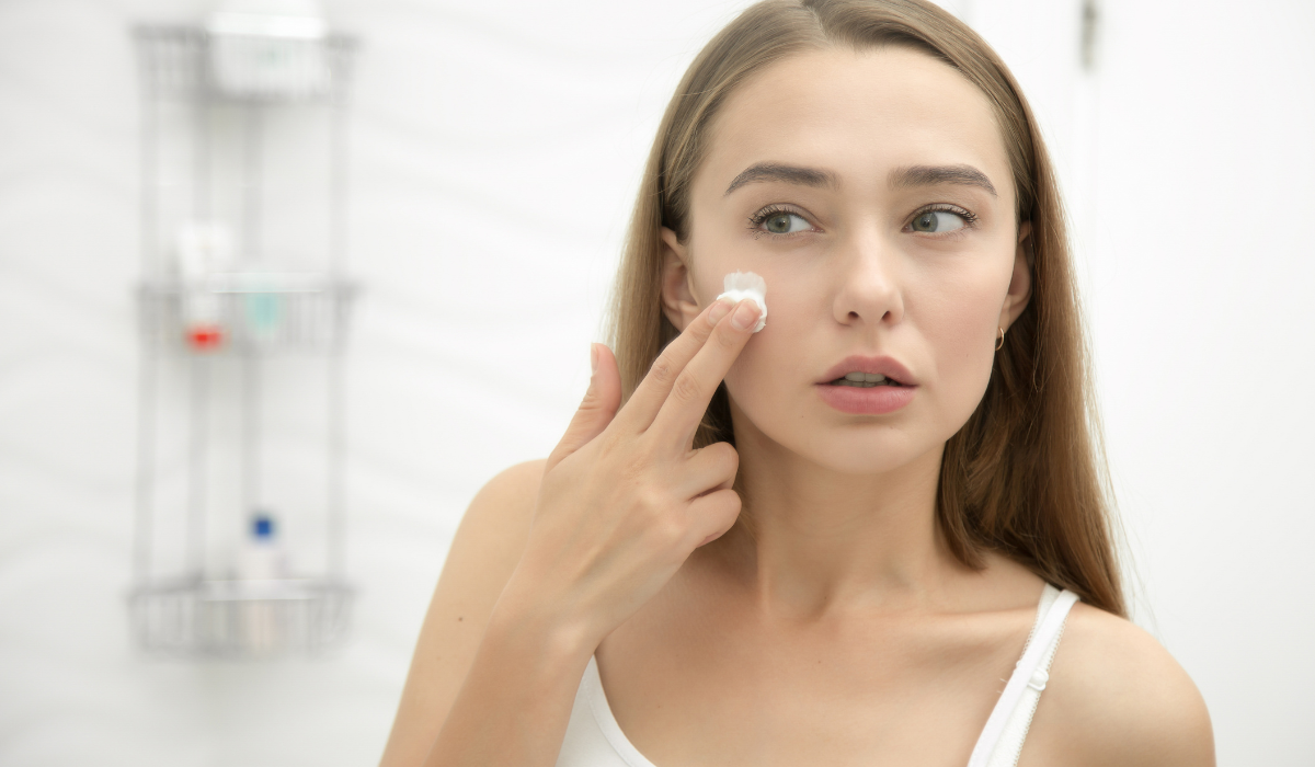 Chica joven aplicándose crema en la cara.